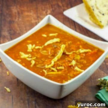 A rich and creamy Carrot Tomato Soup served in a white bowl, resting on a warm brown wooden surface, with a loaf of bread visible in the soft background.