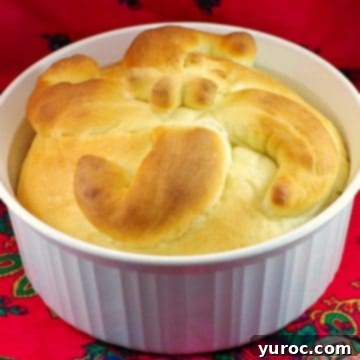 A festive Paska bread, baked to golden perfection, presented in a round white casserole dish on a red patterned surface, ready for celebration.