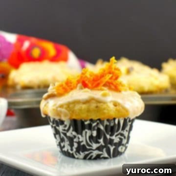 A beautifully glazed carrot cake donut muffin presented on a white plate, with additional muffins visible in the soft background, showcasing their inviting texture.