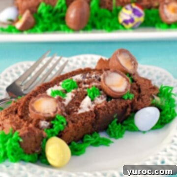 A decadent slice of Easter Swiss Roll Cake resting on a white plate with a delicate lattice trim, accompanied by a fork, with the whole festive cake visible in the background.