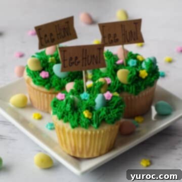 Three delightful Mini Egg cupcakes arranged on a square white plate, with extra mini eggs and charming candy flowers scattered around, creating a festive Easter scene.