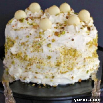 An elegant White Chocolate Pistachio cake proudly displayed on a sleek black stand, ready to be sliced and enjoyed.