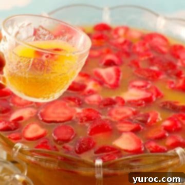 A festive strawberry party punch beautifully presented in a large punch bowl, with a mug of the vibrant drink being held up in the foreground.