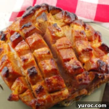 A perfectly cooked Picnic Ham glistening with orange glaze, presented on a rustic platter with a red checkered towel in the background.