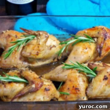Succulent Cornish game hens generously coated with rosemary wine sauce, presented in a glass baking dish, with blue oven mitts blurred in the background.
