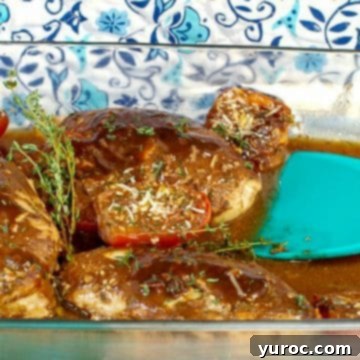 Flavorful Balsamic chicken baked with vibrant tomatoes in a clear glass dish, accompanied by an aqua blue spatula.