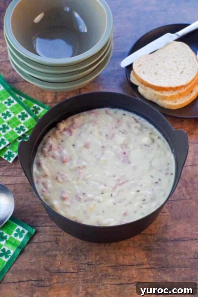 Reuben chowder in a black pot with ladle and clover leaf green and white napkins, sage green bowls and rye bread in the background