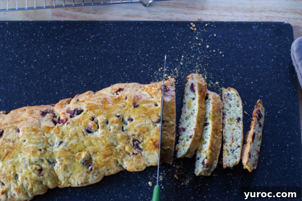 Biscotti loaf being sliced on a black cutting board with a serrated knife, demonstrating the diagonal cut.