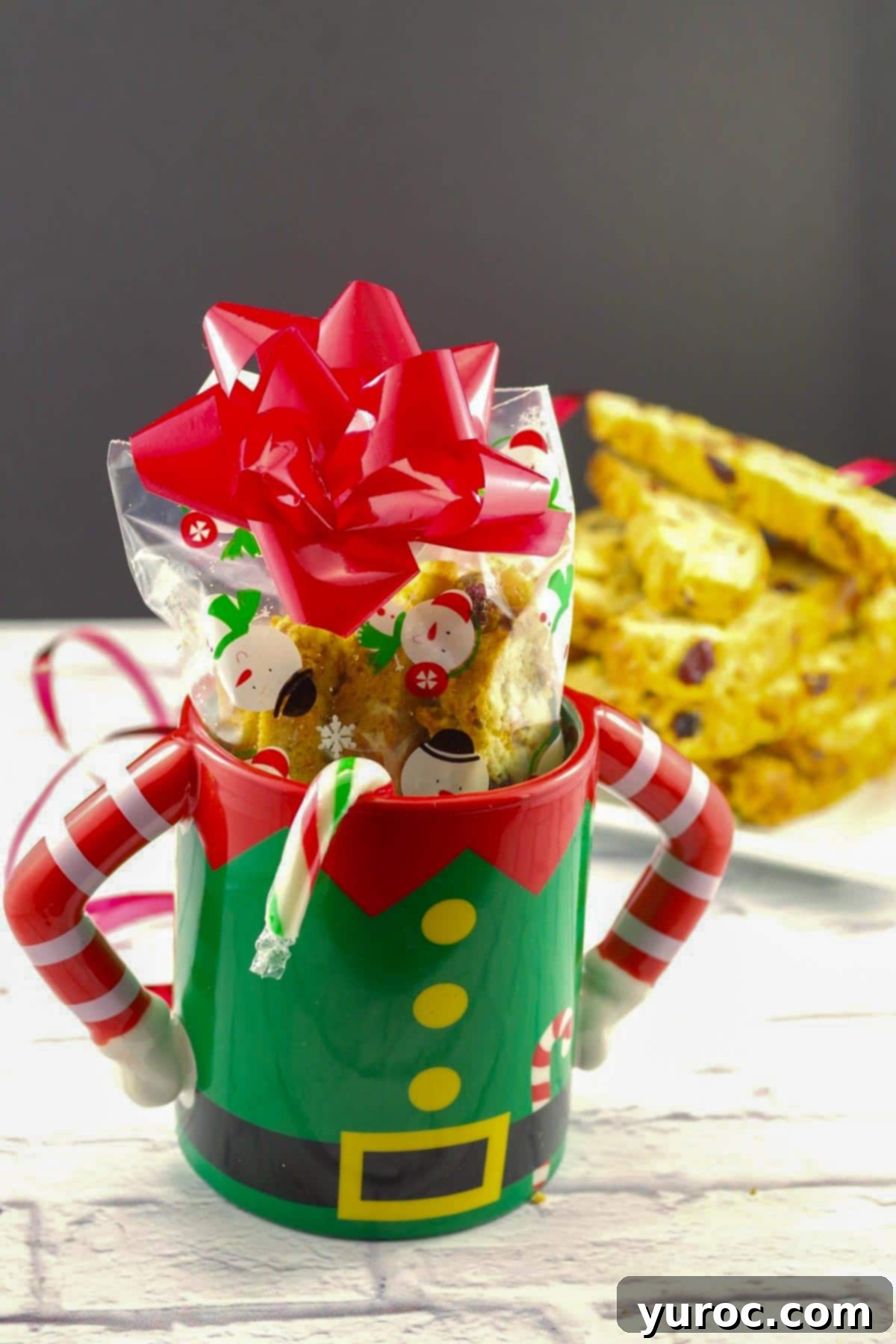 Christmas biscotti in a Christmas mug with a plate of biscotti in the background, beautifully presented for the holidays.