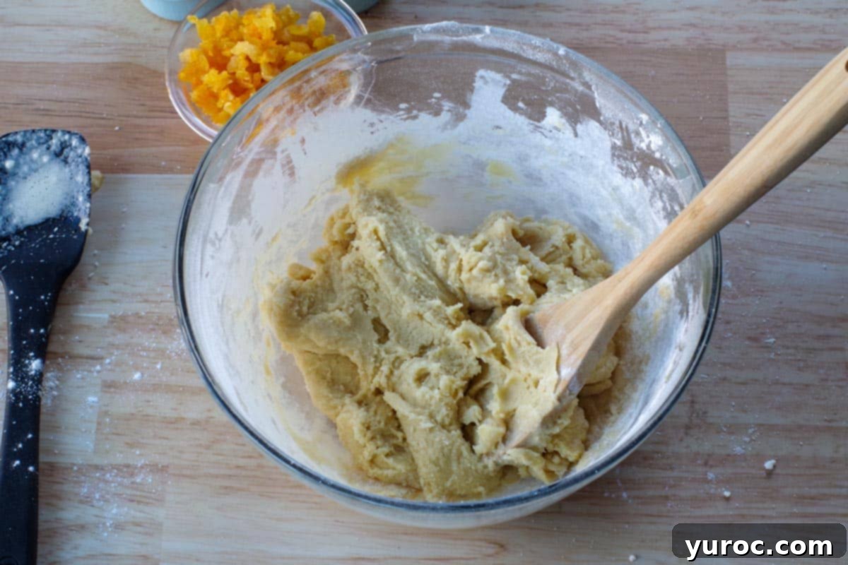 Flour fully mixed into the dough mixture with a wooden spoon in a glass bowl, achieving a uniform consistency.