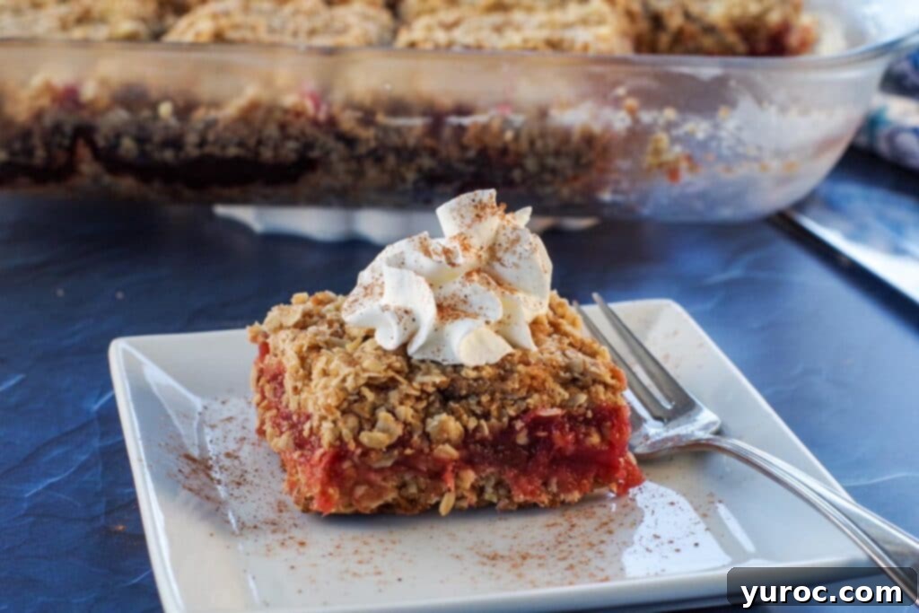 A single rhubarb square on a white plate, with a glass baking dish filled with more rhubarb squares visible in the softened background.