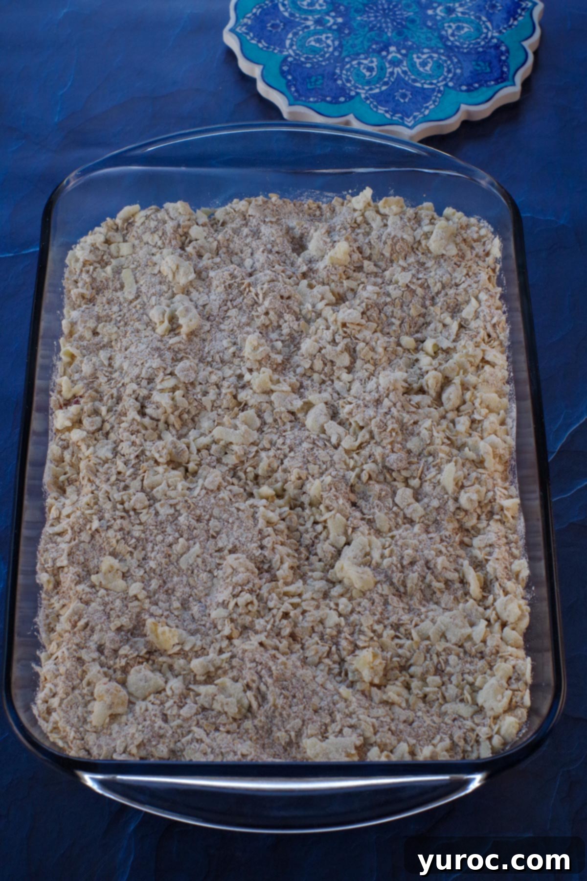 The remaining oatmeal crumble mixture sprinkled over the rhubarb filling in the baking pan, creating the top layer of the bars.