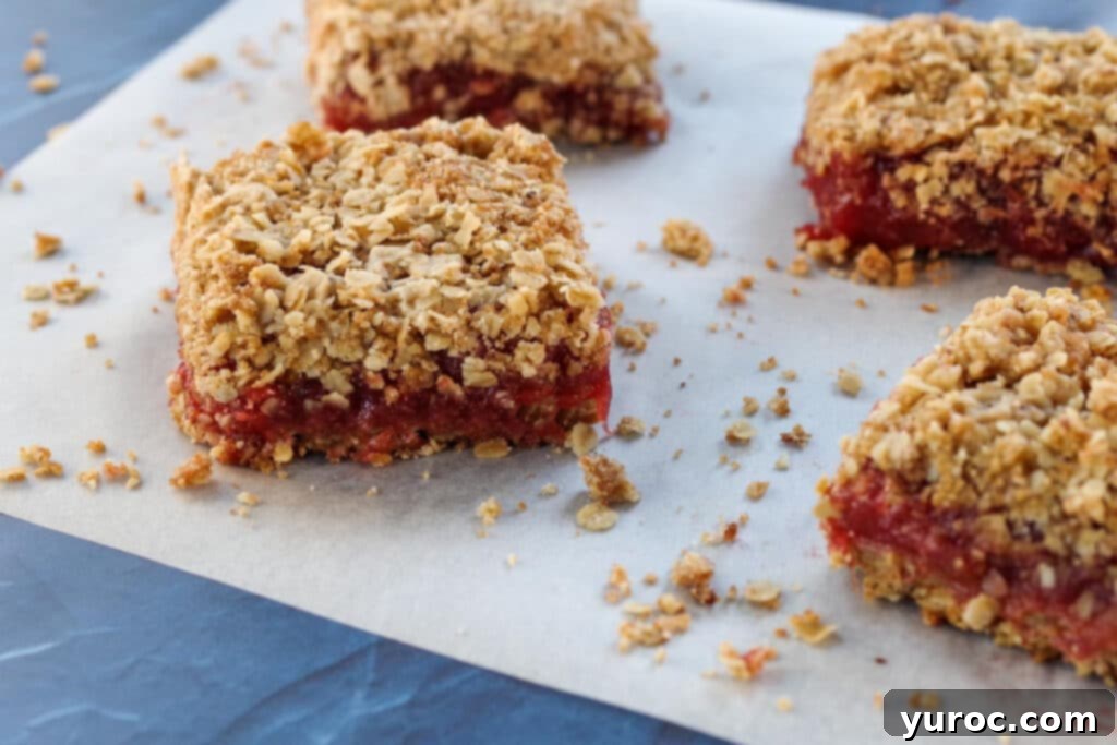 Several golden brown rhubarb crumble bars arranged artfully on a piece of parchment paper, highlighting their crumbly top and thick filling.