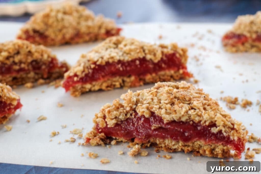 Freshly baked rhubarb bars, precisely cut into neat triangles, arranged on a sheet of parchment paper, highlighting their golden crumble topping and pink filling.