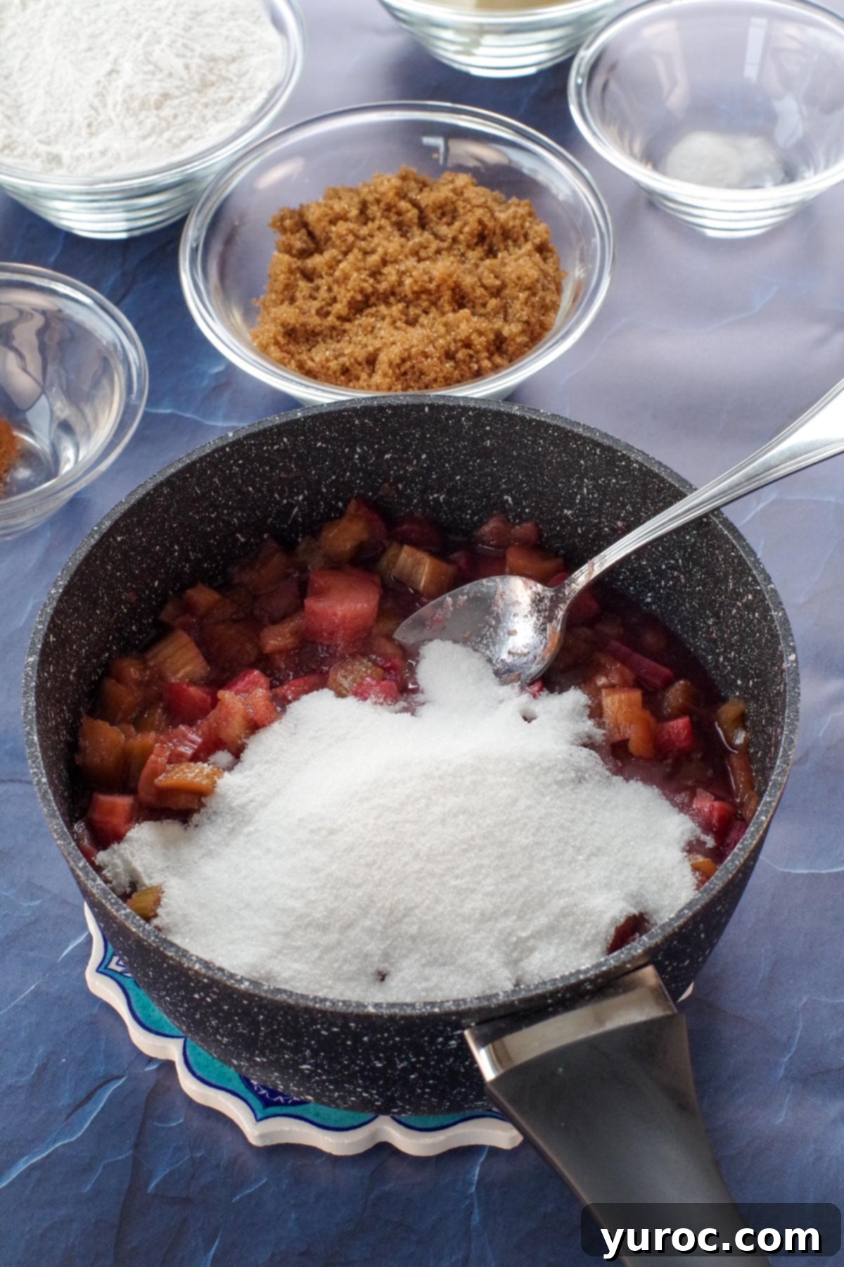 Chopped rhubarb cooking in a saucepan with sugar and lemon zest, beginning to soften and release juices.