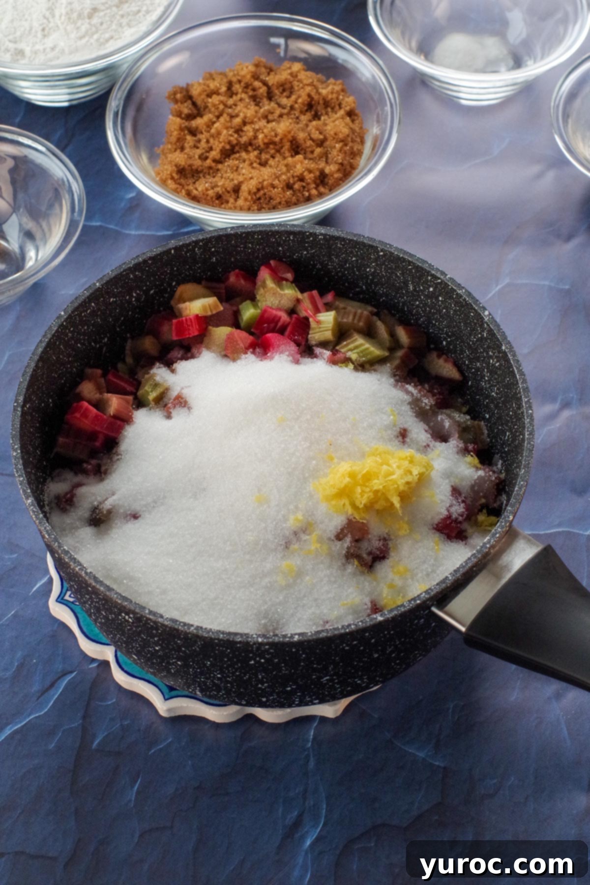 Cooked rhubarb mixture in a saucepan, now combined with the remaining sugar and cornstarch, appearing thicker.