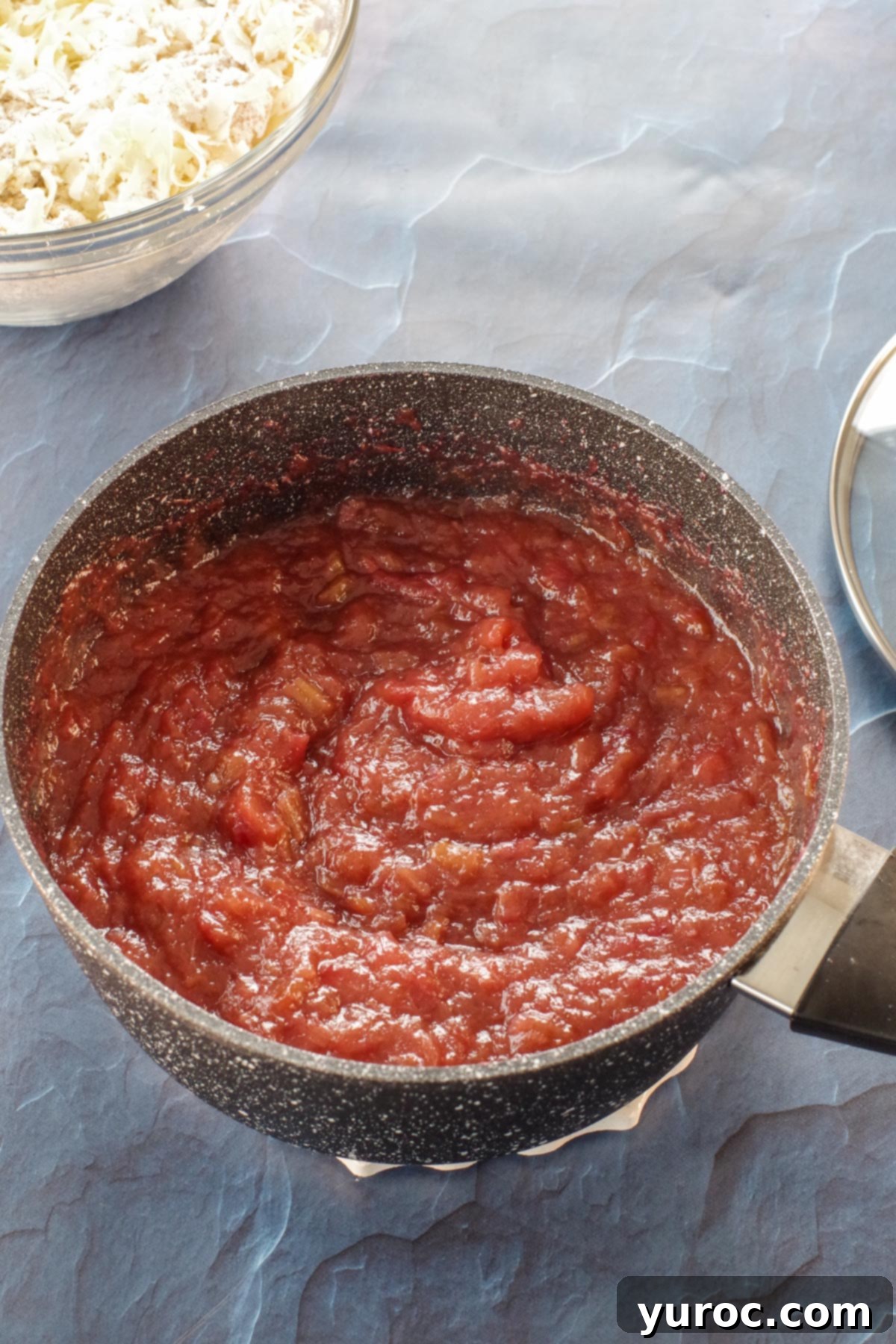 A close-up of the fully cooked rhubarb filling in a saucepan, showing its broken-down consistency and natural brownish-pink color before food coloring is added.