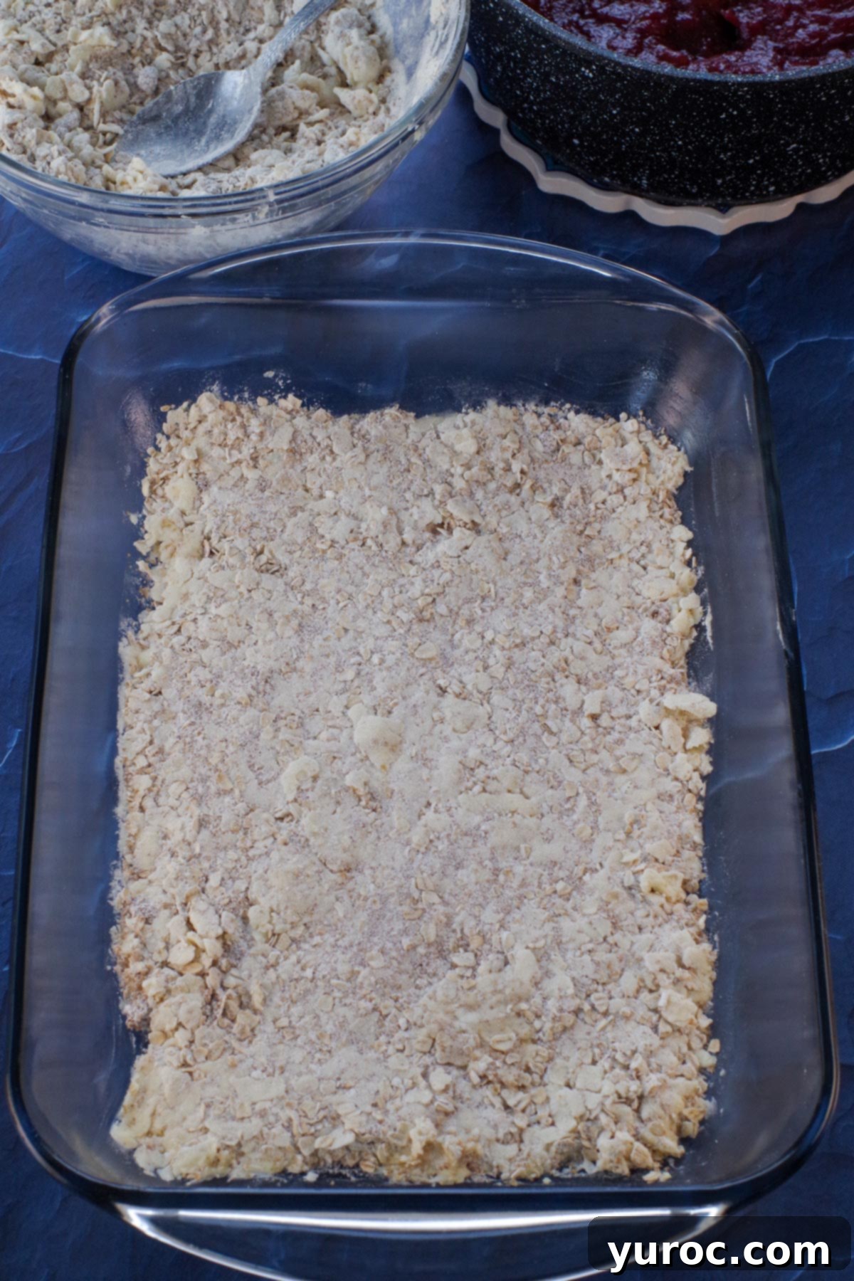 Half of the oatmeal crumb mixture evenly pressed into the bottom of a 9x13 inch baking pan, forming the base for the rhubarb bars.