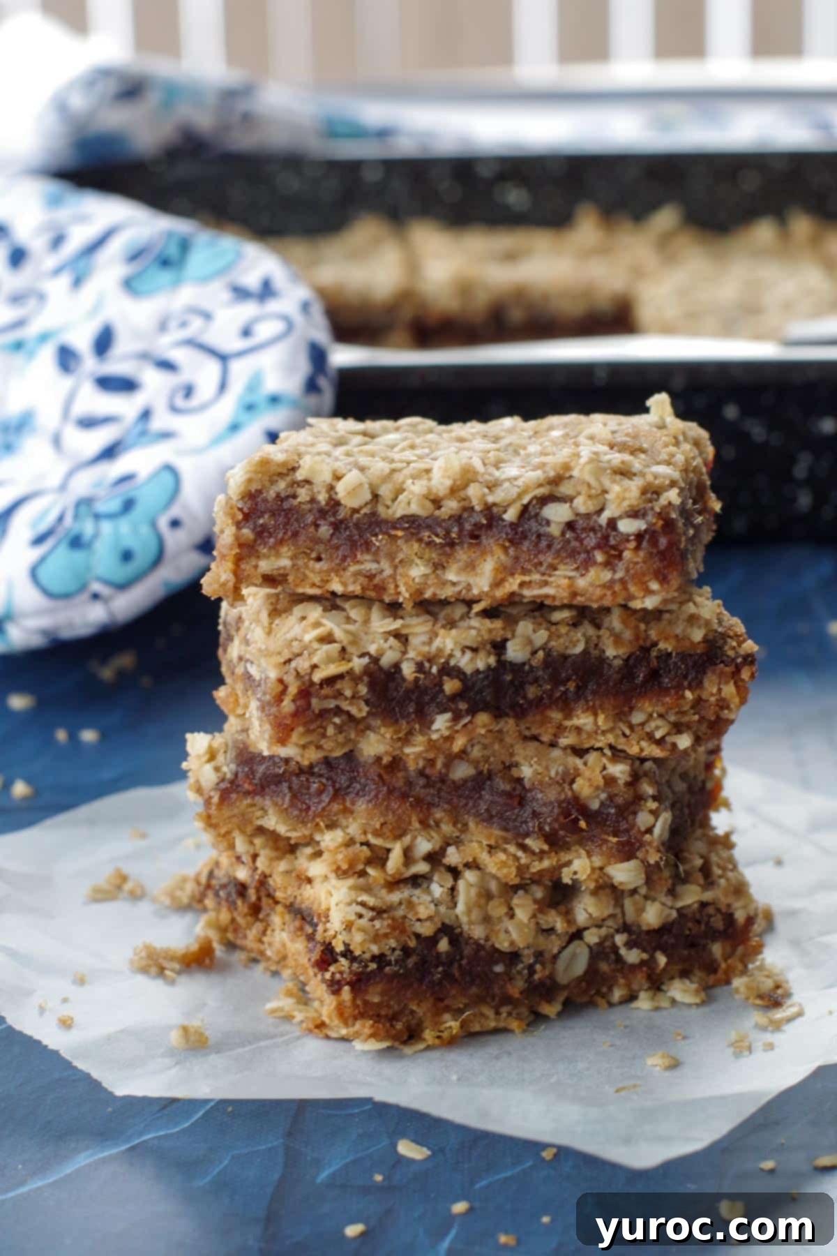 4 date squares piled up on a piece of parchment paper with a blue flowered oven mitt in the background