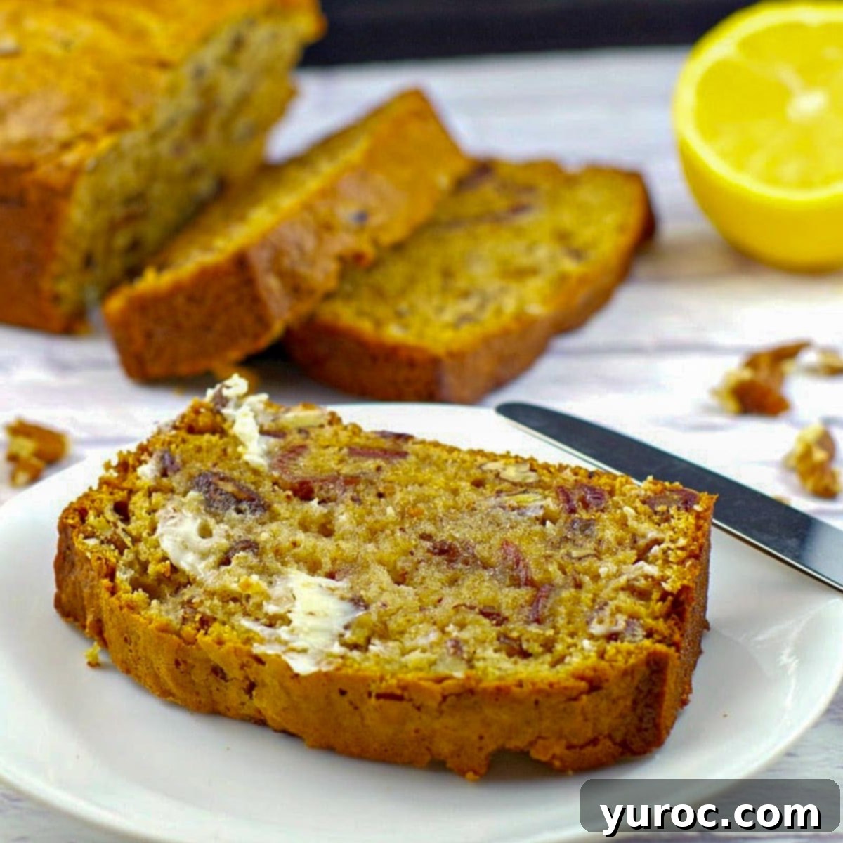 date nut loaf slice on white plate with remainder of loaf and sliced lemons in background