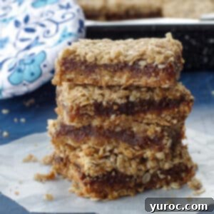 4 date squares piled up on a piece of parchment paper with a blue flowered oven mitt in the background