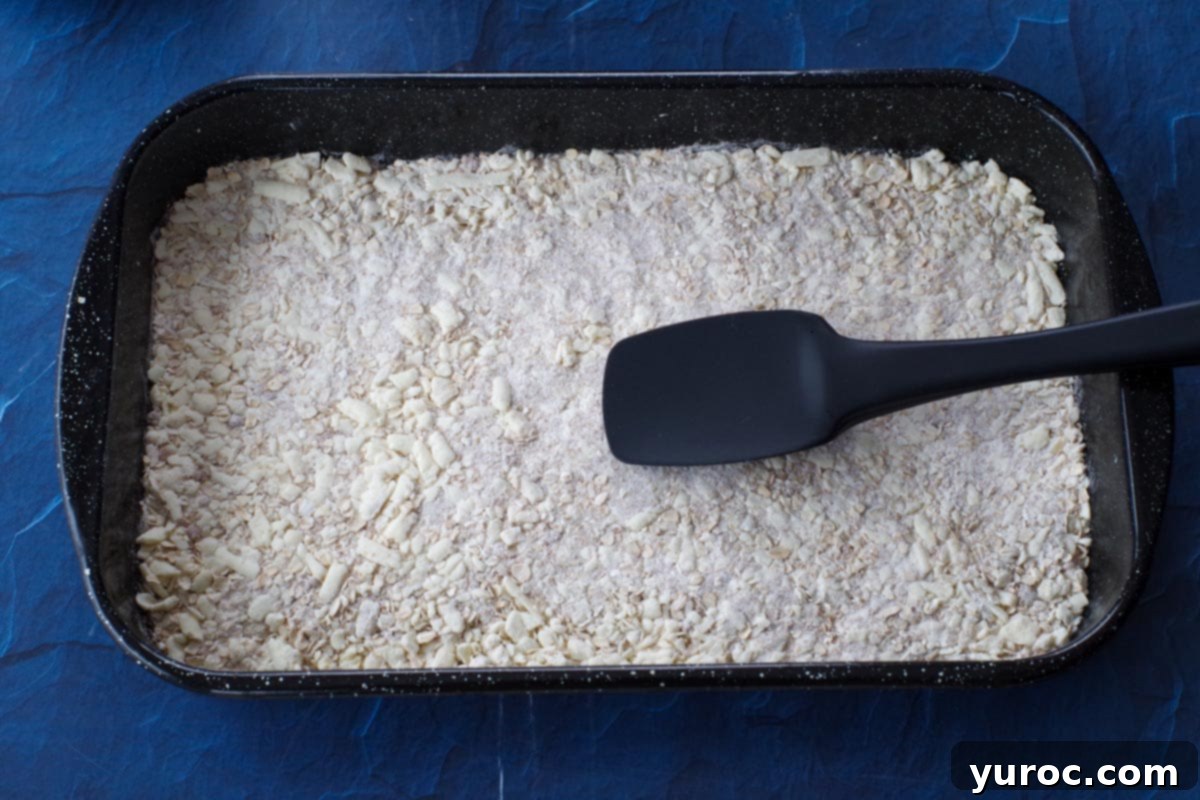 flour and oat mixture being pressed into the bottom of a pan with spatula