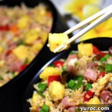Hawaiian pineapple fried rice in a black bowl with some being lifted out with chopsticks