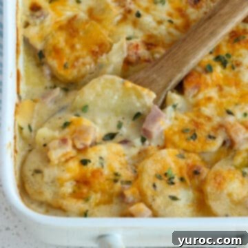 scalloped potatoes and ham in a white casserole dish, with a wooden spoon