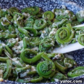 15 Creative Fiddlehead Dishes 6 Cheesy Sauteed fiddleheads in a pan with a white spatula