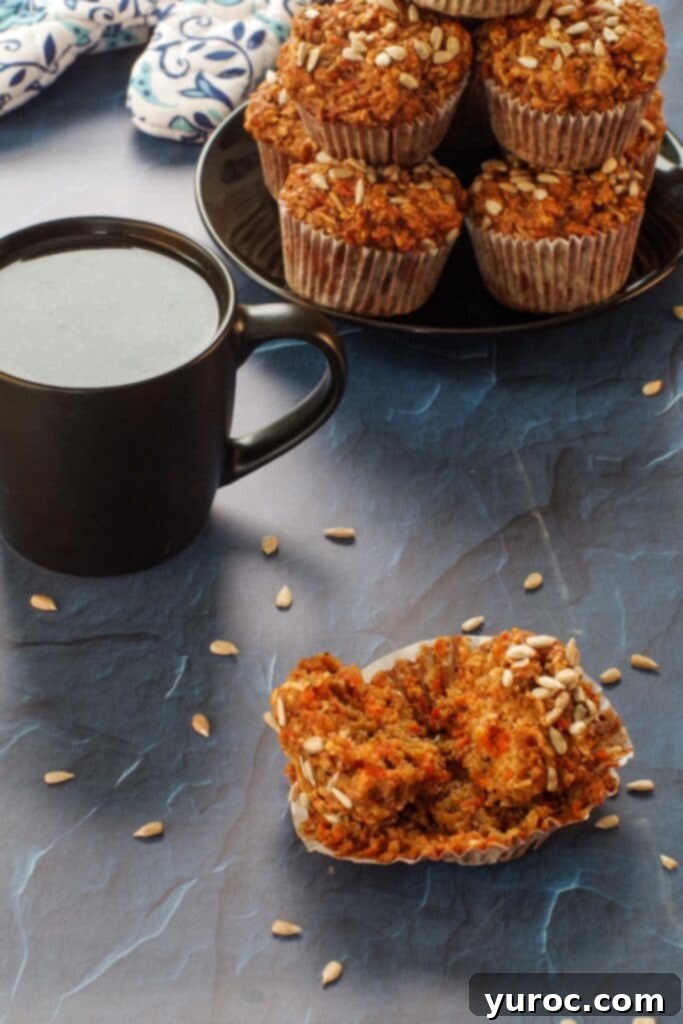 morning glory muffin cut in half on wrapper with black cup of coffee and stack of muffins on black plate, in background