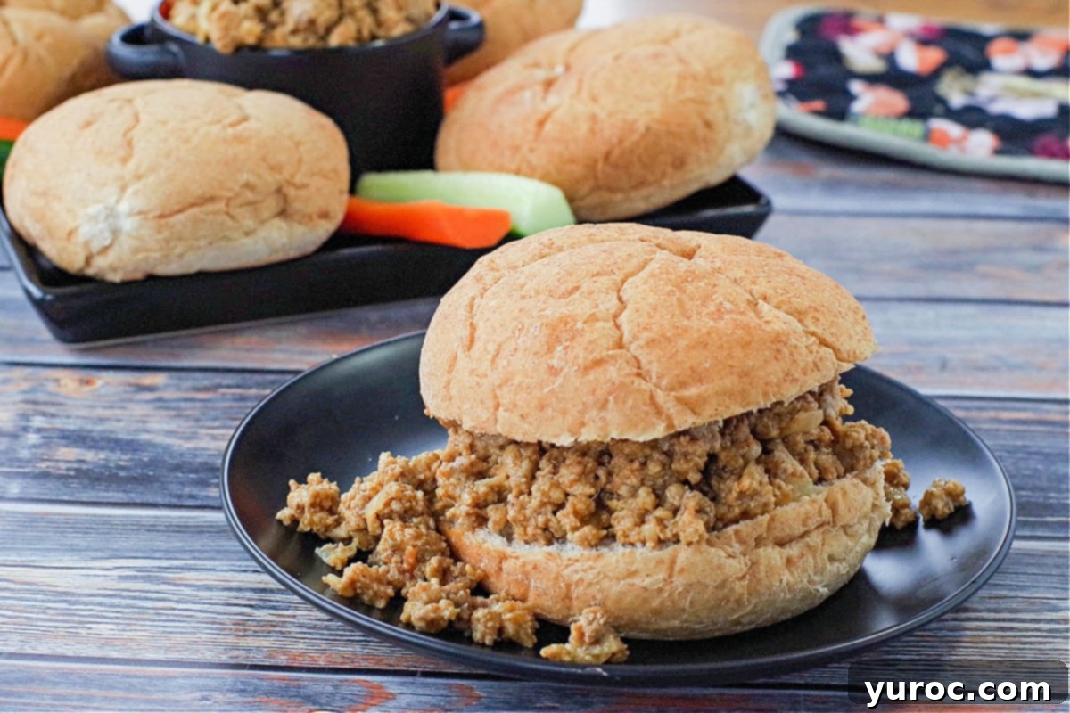 Guilt-Free Turkey Sloppy Joes 3 ground turkey sloppy joes on a black plate with a tray of buns, veggies and sloppy joes in the background