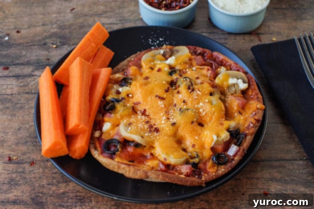 A healthy pita pizza on a black plate with carrot sticks and parsley garnish.
