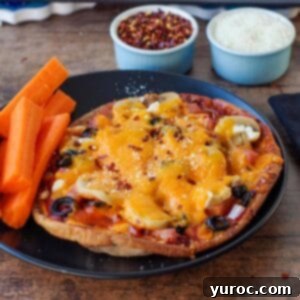 A perfectly baked healthy pita pizza on a black plate with carrot sticks.