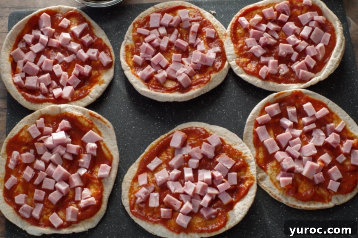 Chopped ham being sprinkled on pita pizzas, illustrating step 2.