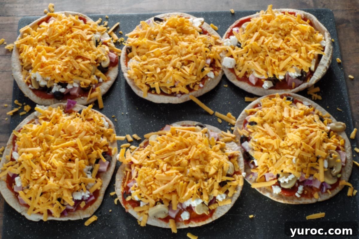 Pita pizzas with cheddar cheese sprinkled on top, ready for baking, illustrating step 4.