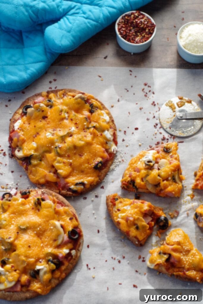 Pita pizzas on parchment paper, with one cut into 4 pieces, ready to be served.