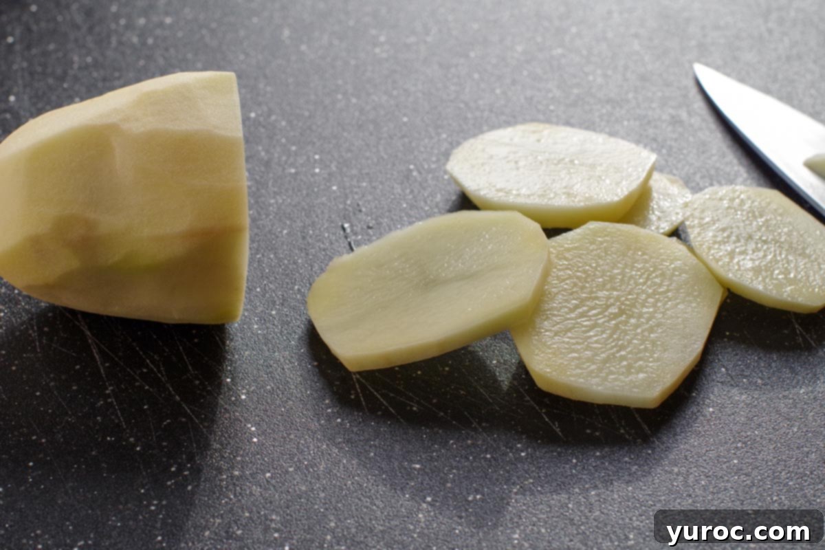 Thinly sliced potatoes, precisely cut into ⅛ inch rounds, neatly arranged on a sleek black cutting board, ready for the next step in the Perogy Pizza preparation.
