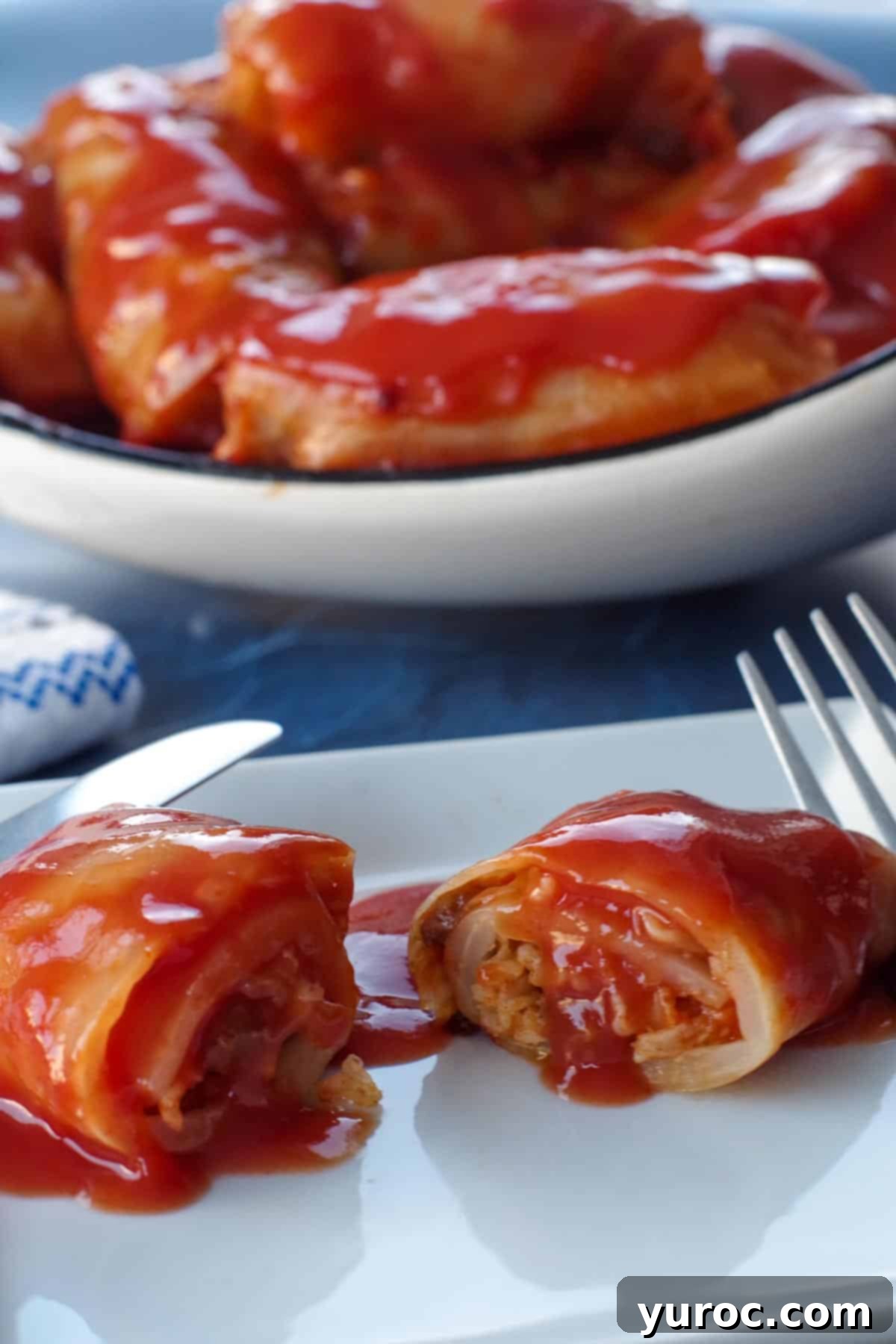 Ukrainian cabbage roll, on a white plate, cut in half, with dish of more cabbage rolls in the background
