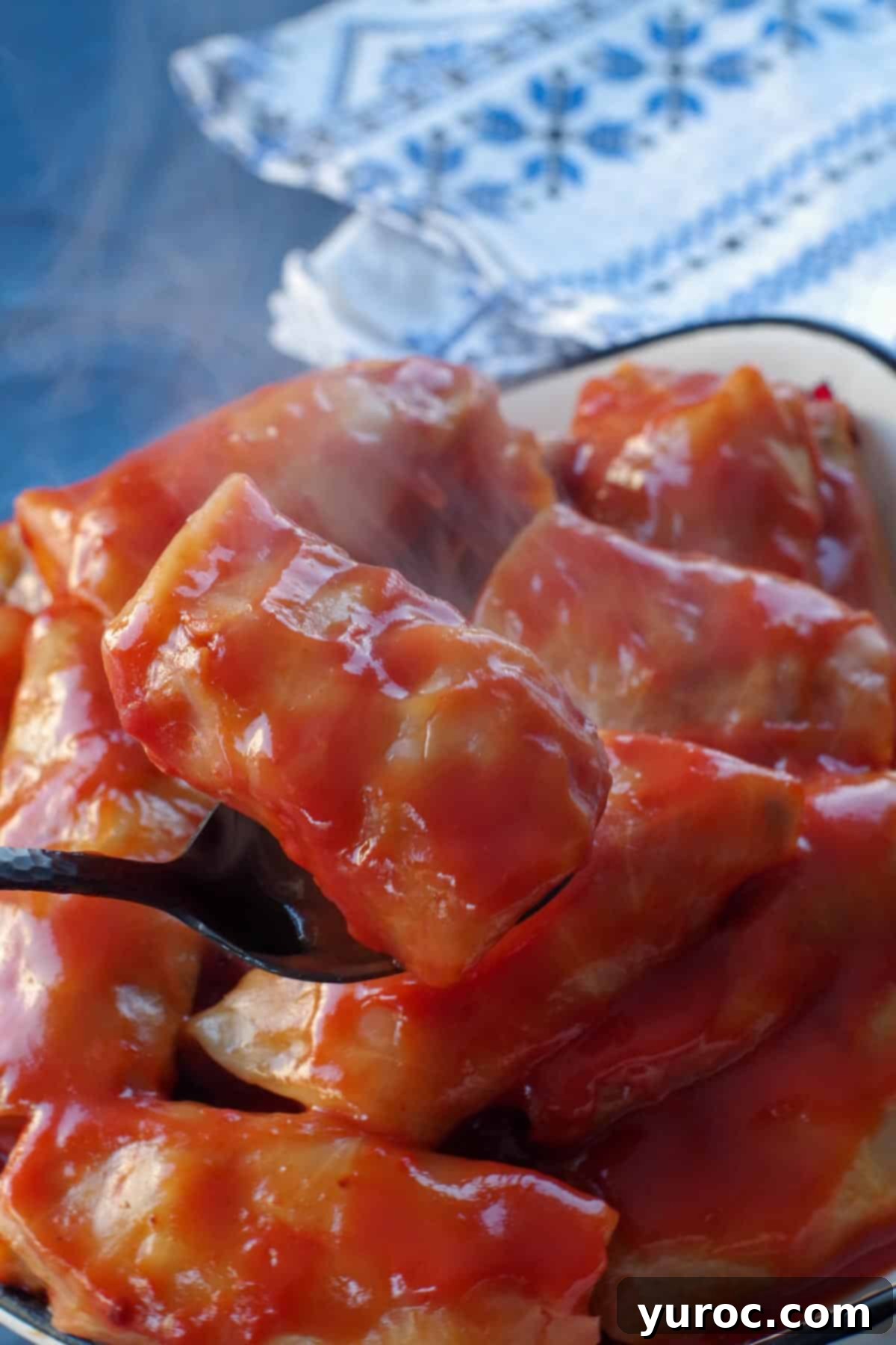 cabbage roll being held up on a spoon, over a dish of more cabbage rolls