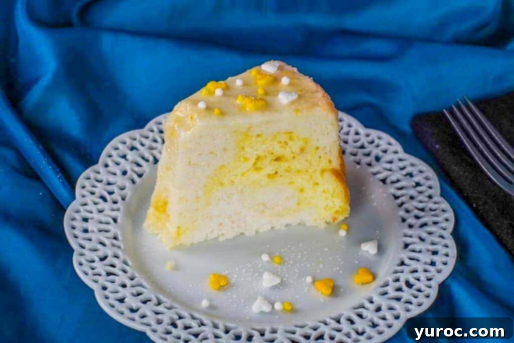 a slice of daffodil cake on a white plate with lattice trim and a blue material background