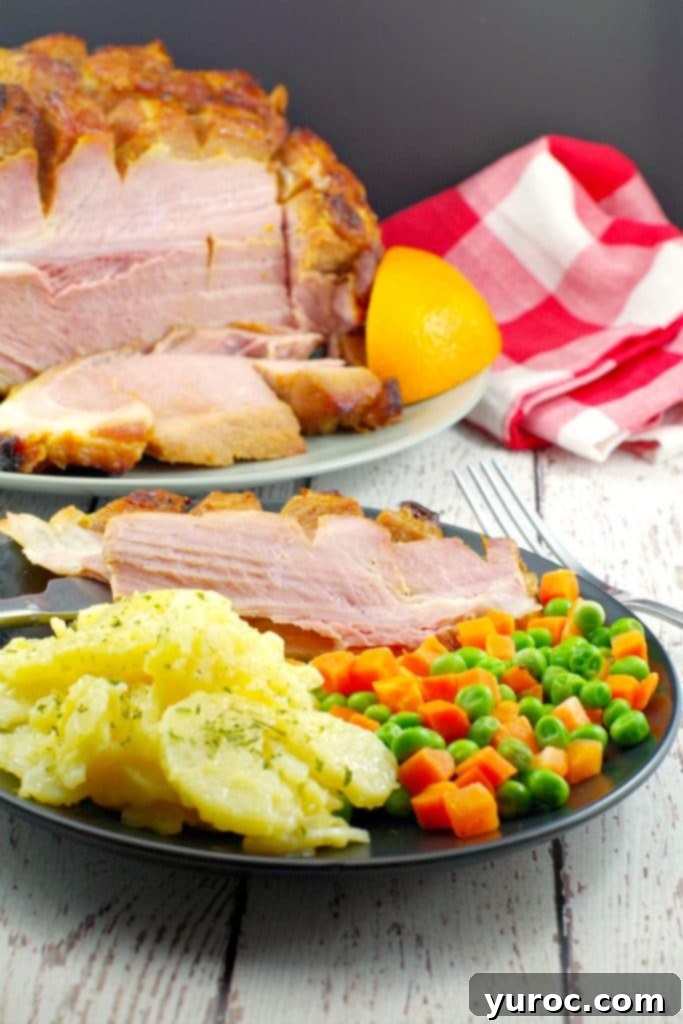 Sliced picnic ham on a plate with scalloped potatoes and veggies with whole ham in background
