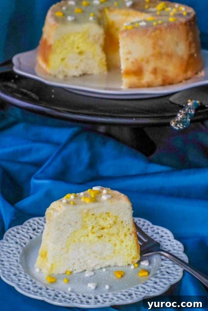 a slice of daffodil cake on a white plate with lattice trim and whole cake (with slice removed in background and a blue material background