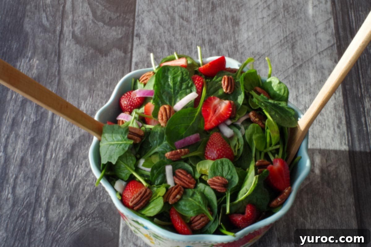 strawberries, spinach, red onion and toasted pecans in a large flowered salad bowl with wooden utentils