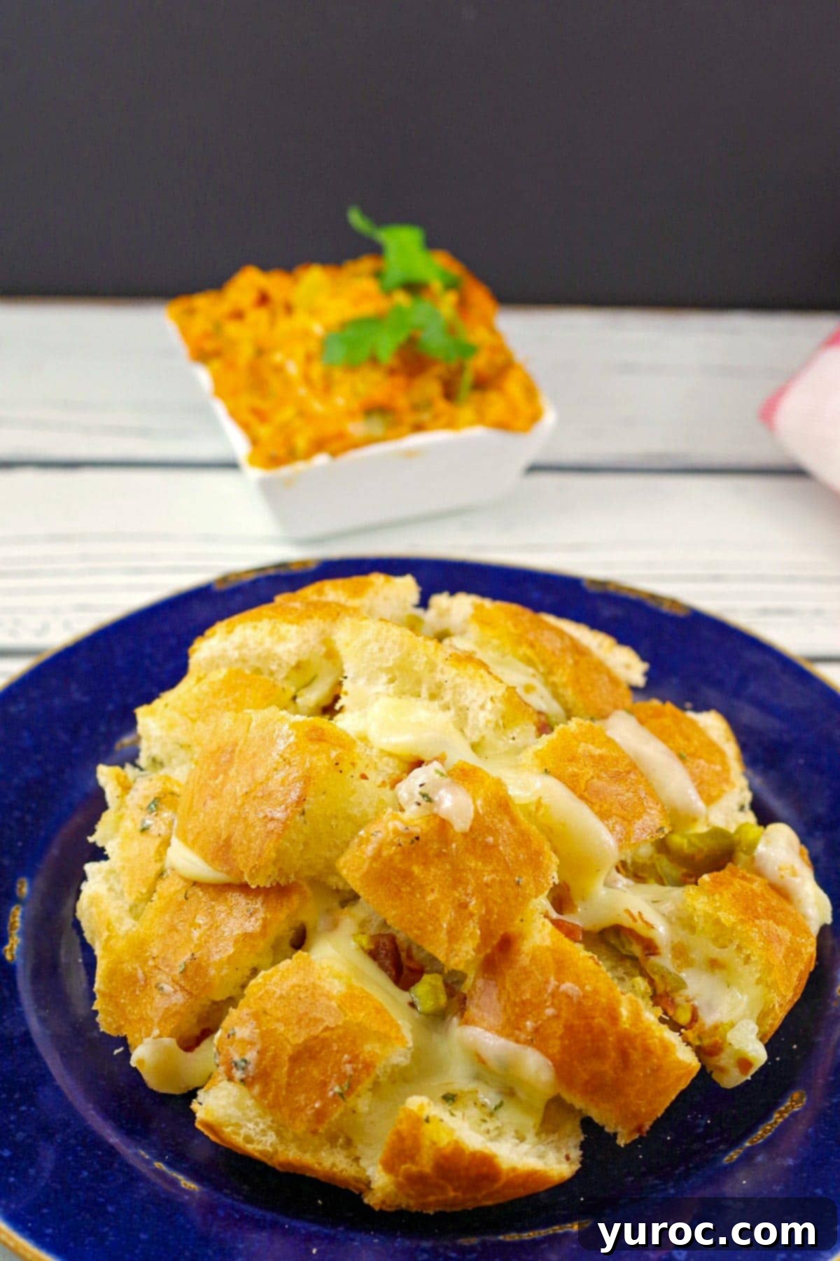 cheese and bacon pull apart bread on a blue plate with small bowl of dip in the background