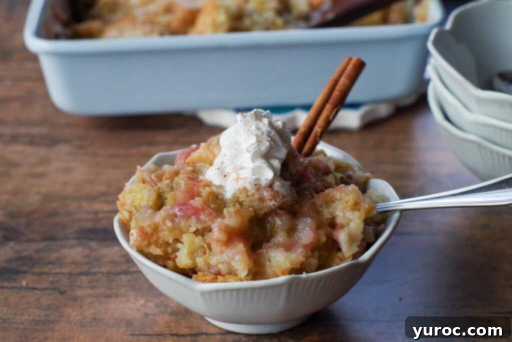 A beautiful white petal bowl filled with fresh rhubarb stalks, accompanied by a fragrant cinnamon stick, with a golden-baked sticky rhubarb pudding in a pan blurred in the background, hinting at the deliciousness to come.