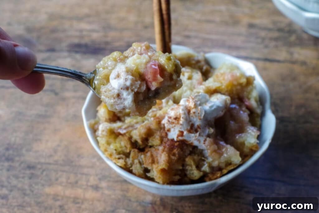 A close-up shot of sticky rhubarb pudding served in a white bowl, with a spoonful being lifted out, showcasing the moist cake and luscious, gooey rhubarb sauce.