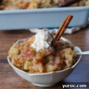 A white petal bowl filled with fresh rhubarb stalks, accompanied by a fragrant cinnamon stick, with a golden-baked sticky rhubarb pudding in a pan blurred in the background, hinting at the deliciousness to come.