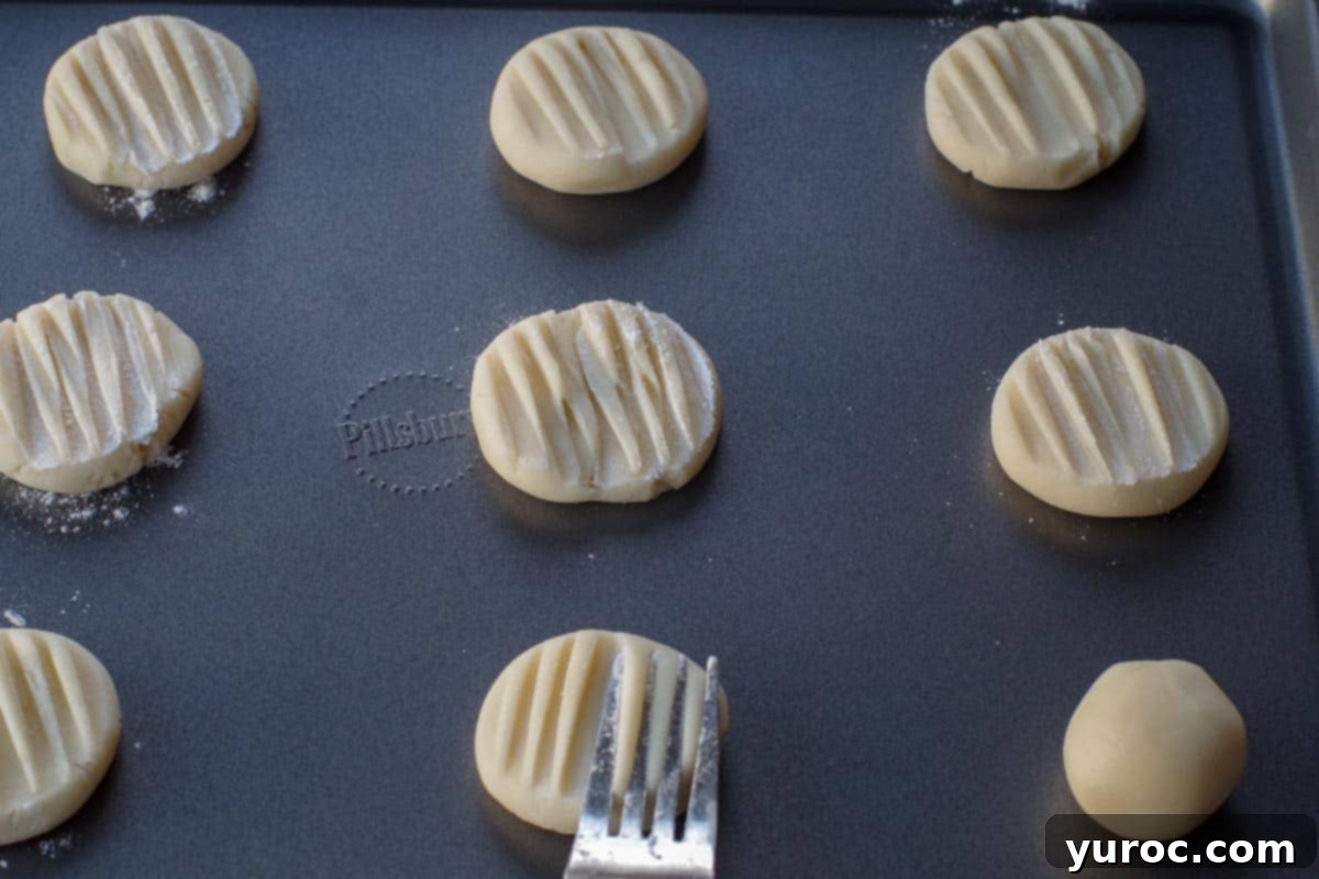 cookie dough balls being pressed with floured tines of a fork on a baking sheet