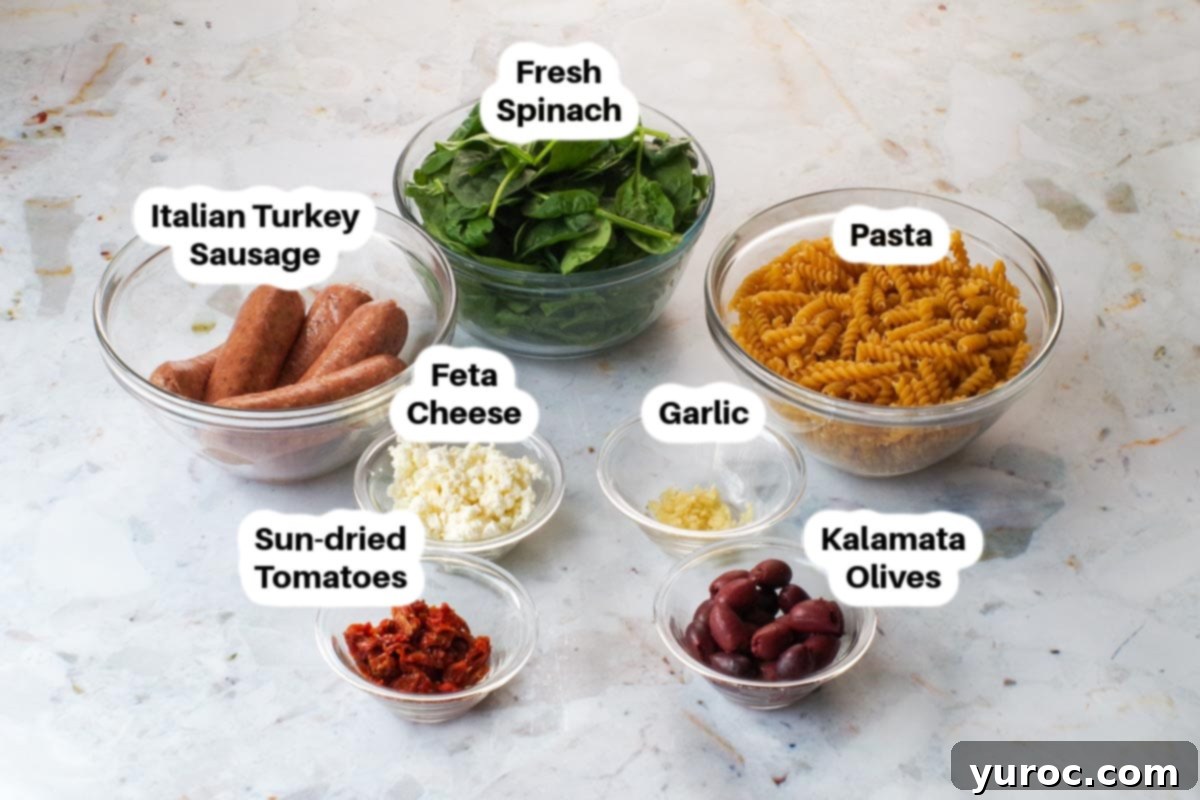 Sun-Kissed Aegean Pasta 3 Ingredients for Greek pasta toss laid out in glass bowls, including pasta, sausage, spinach, olives, sun-dried tomatoes, and feta cheese.