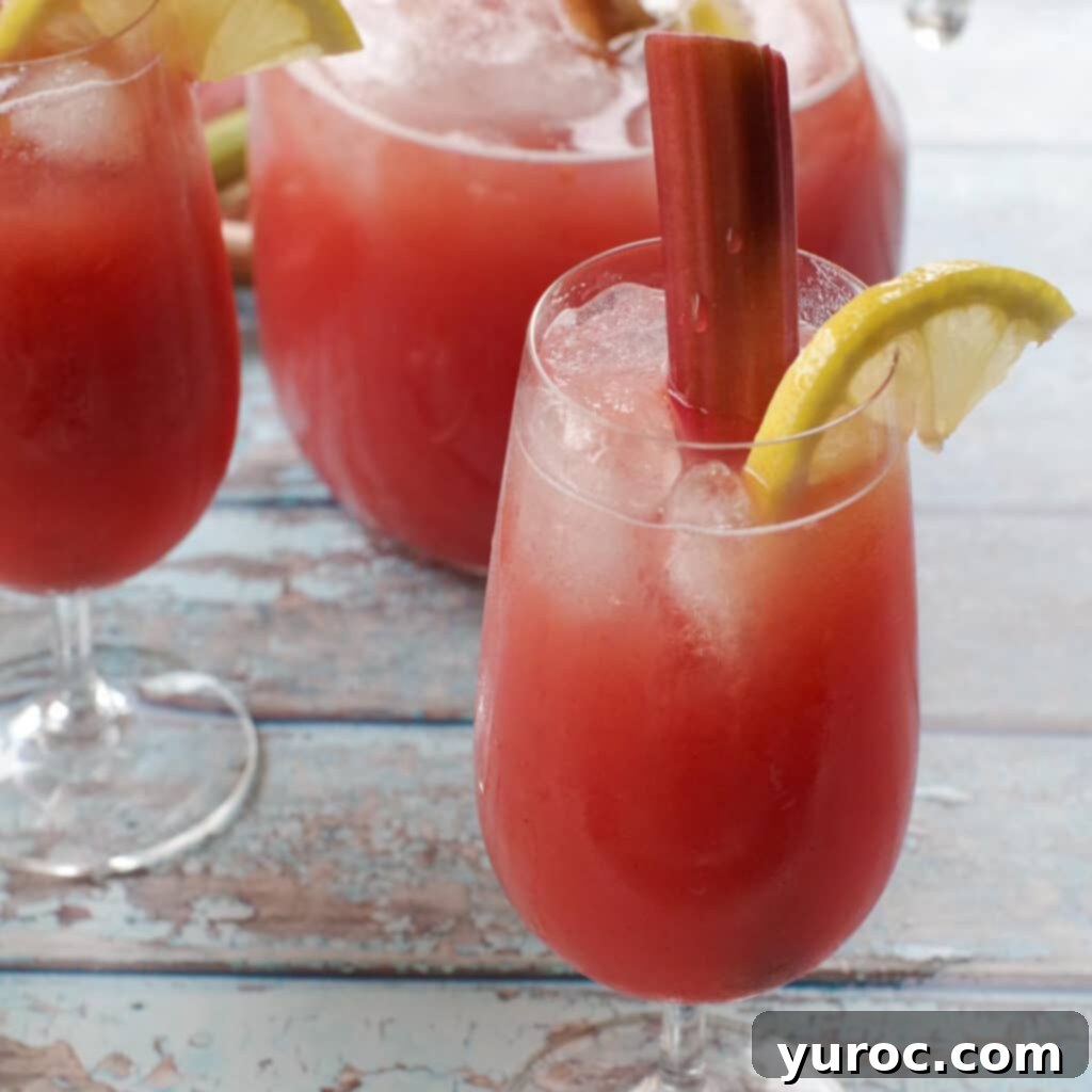 Refreshing rhubarb lemonade served in a tall glass, with a pitcher and another glass in the background, highlighting a delicious use for stewed rhubarb.